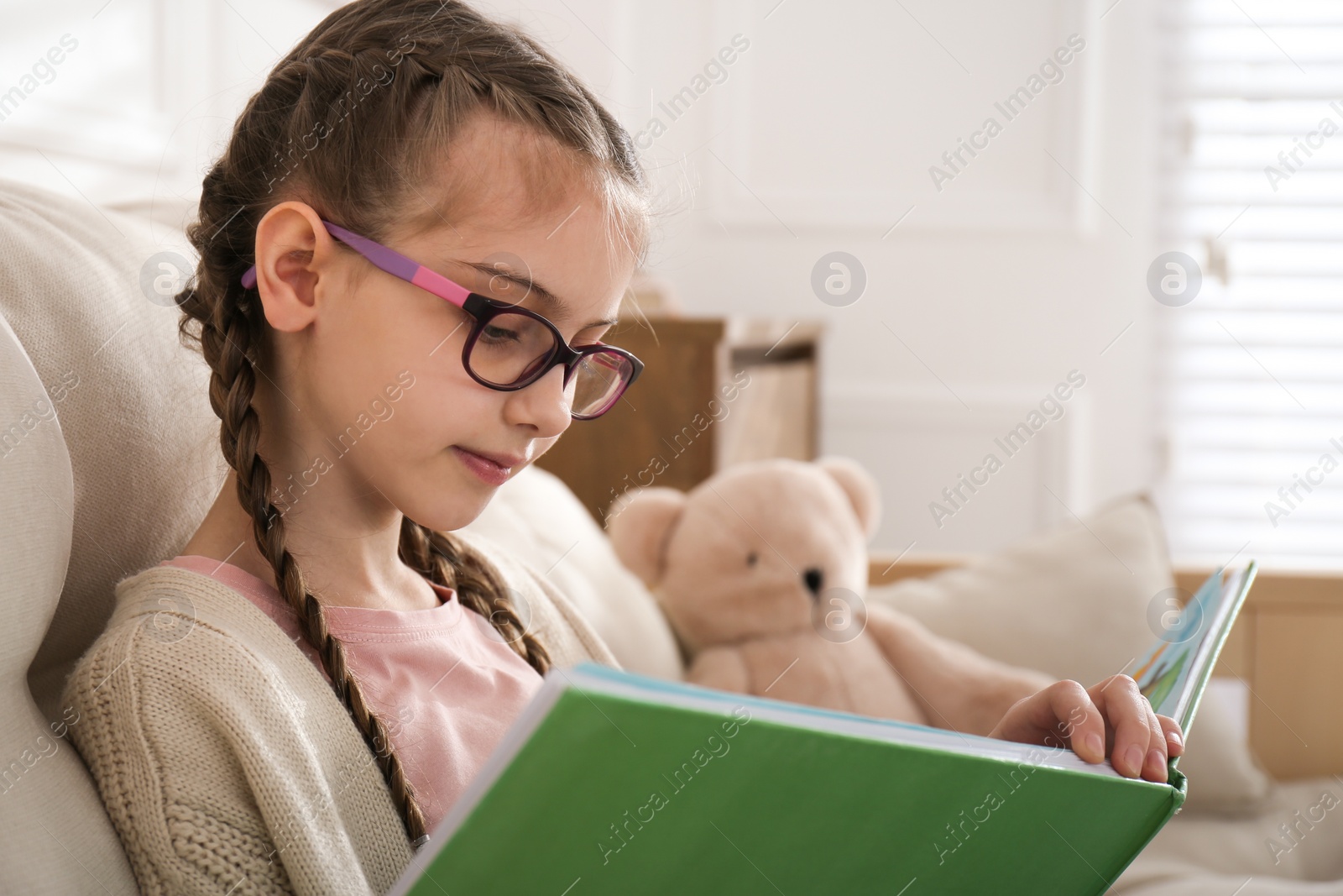 Photo of Cute little girl reading book on sofa at home