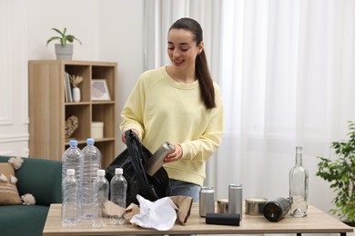 Photo of Smiling woman with plastic bag separating garbage in room