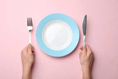 Woman with fork, knife and empty plate on color background, top view