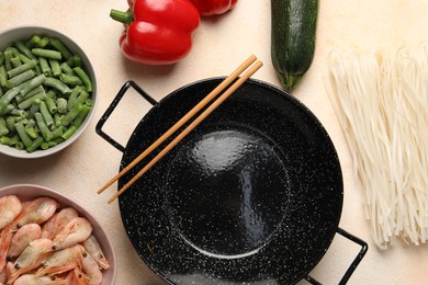 Black wok, chopsticks and products on color table, flat lay