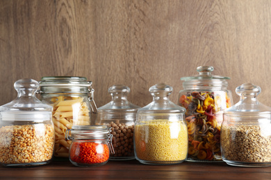 Photo of Glass jars with different types of groats and pasta on wooden table