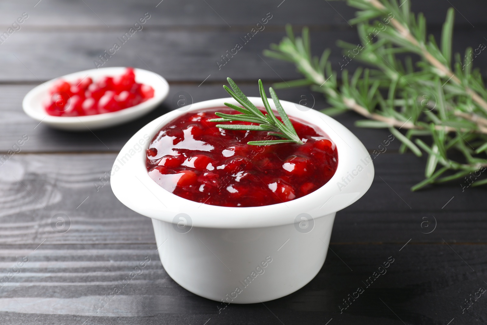 Photo of Fresh cranberry sauce in bowl and rosemary on black wooden table, closeup