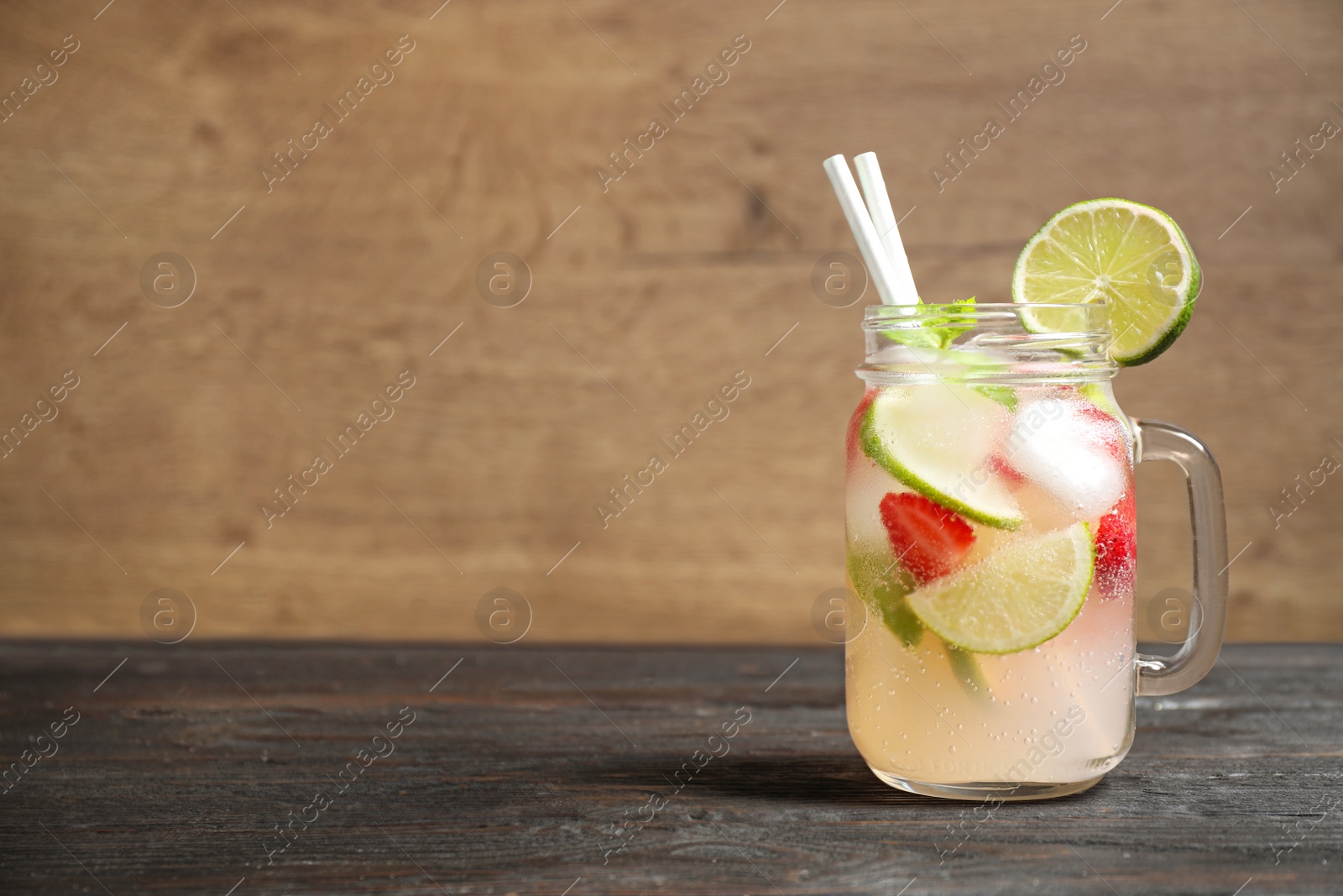 Photo of Mason jar with refreshing drink on table against wooden background. Space for text