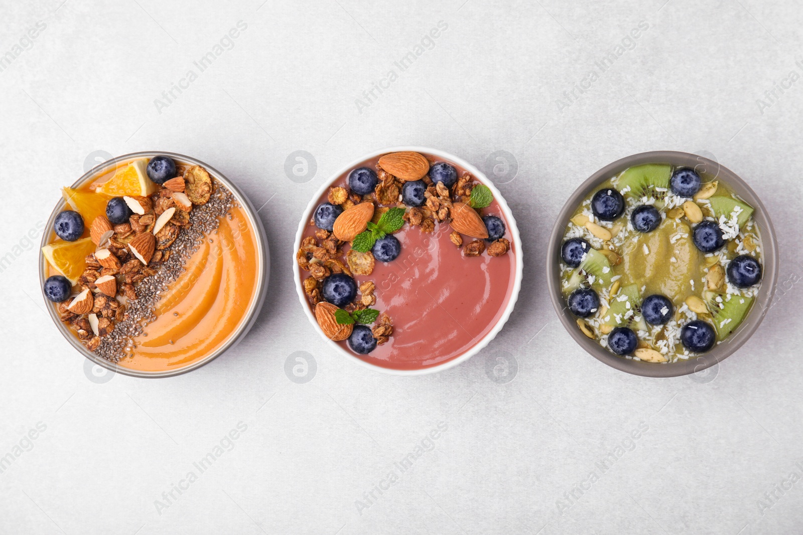 Photo of Bowls with different delicious fruit smoothies on white background, flat lay