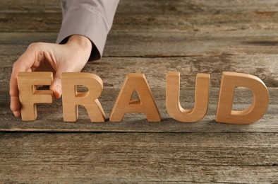 Photo of Woman making word Fraud with wooden letters at table, closeup