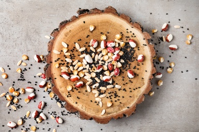 Mixed vegetable seeds and wooden log on grey background, flat lay