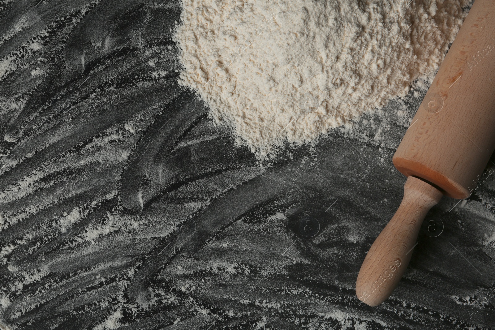 Photo of Flour and rolling pin on black table, top view. Space for text