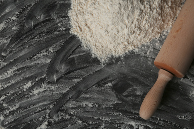 Flour and rolling pin on black table, top view. Space for text