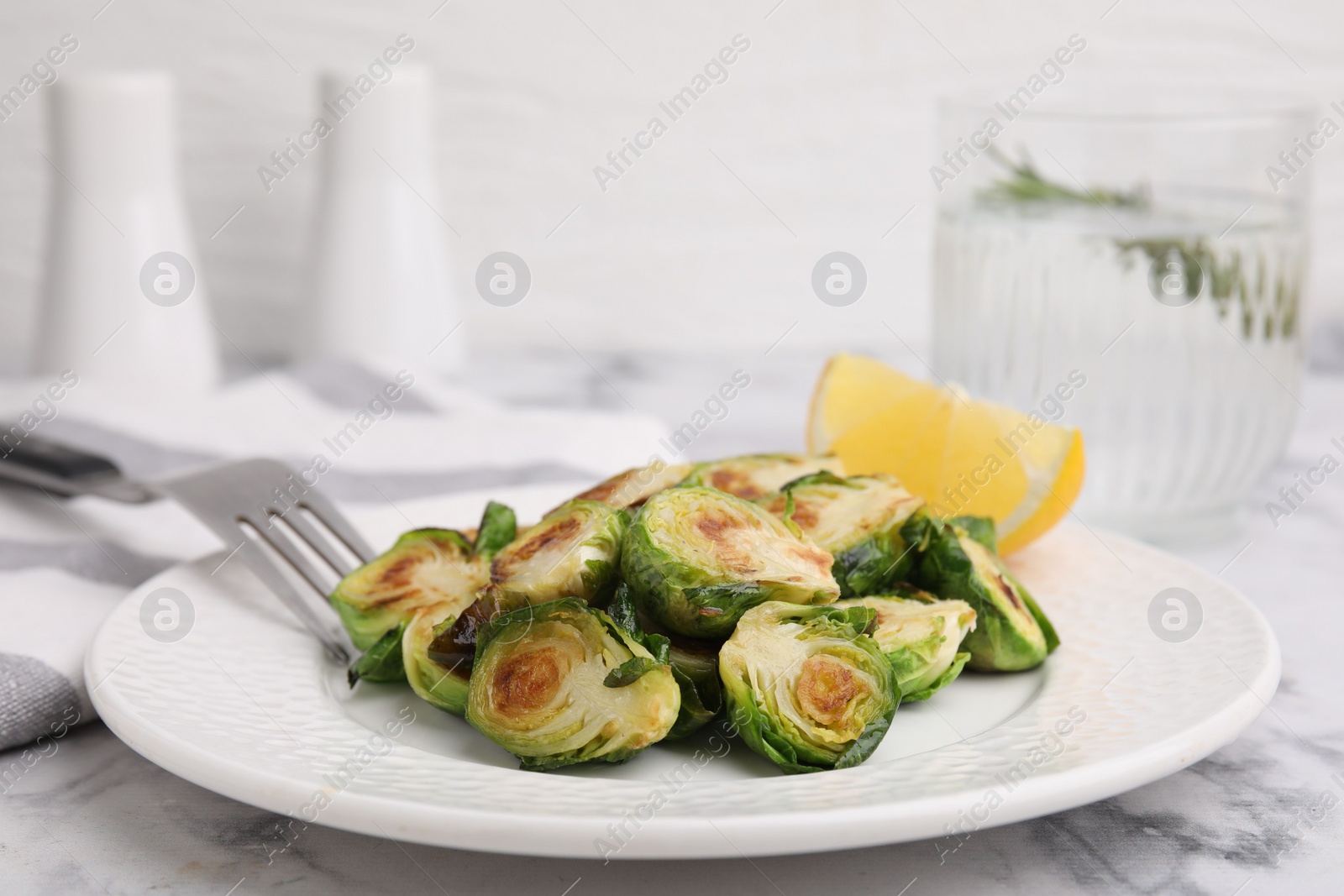 Photo of Delicious roasted Brussels sprouts and slice of lemon on white marble table, closeup