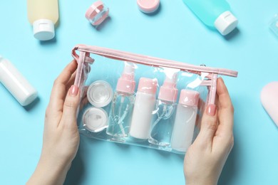 Cosmetic travel kit. Woman with plastic bag and small containers of personal care products on light blue background, top view