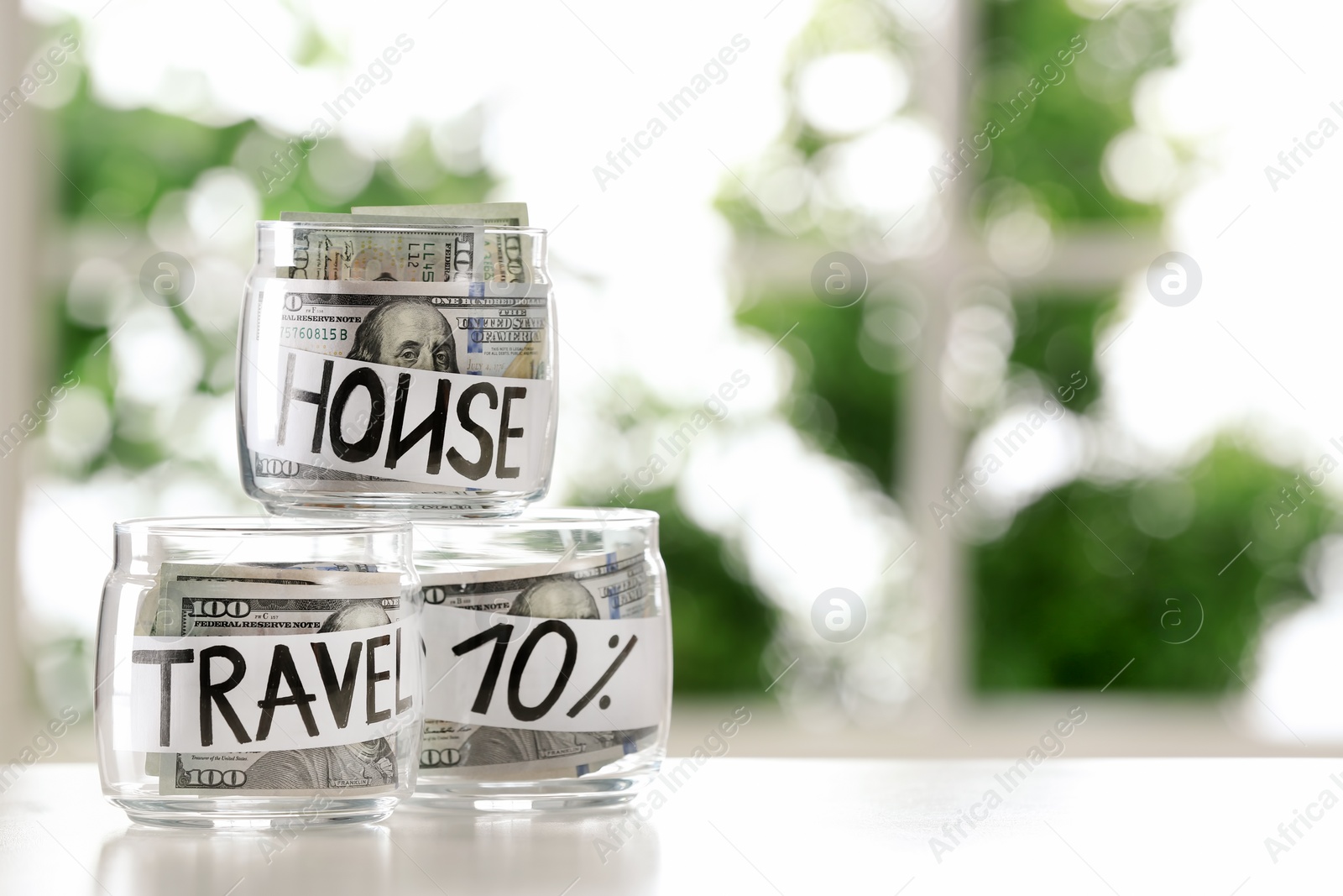 Photo of Glass jars with money for different needs on table against blurred background, space for text