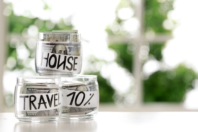 Glass jars with money for different needs on table against blurred background, space for text