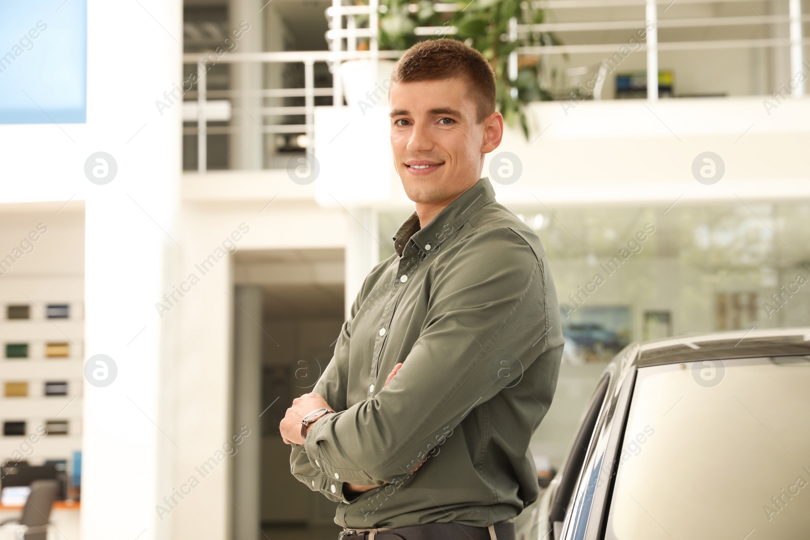 Photo of Young man near new car in modern auto dealership