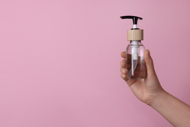 Photo of Woman holding bottle of cosmetic product on pink background, closeup. Space for text