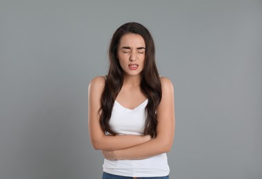 Young woman suffering from stomach ache on grey background. Food poisoning