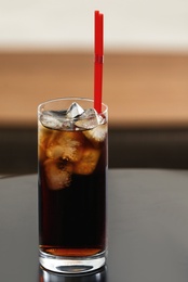 Photo of Glass of cola with ice on table against blurred background