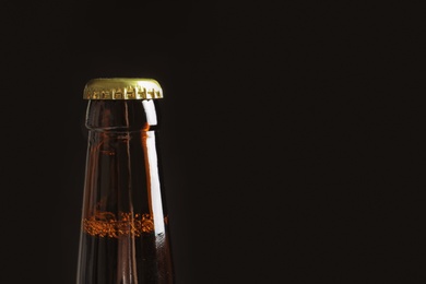 Photo of Bottle of tasty cold beer on black background, closeup