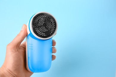 Woman holding modern fabric shaver on light blue background, closeup. Space for text