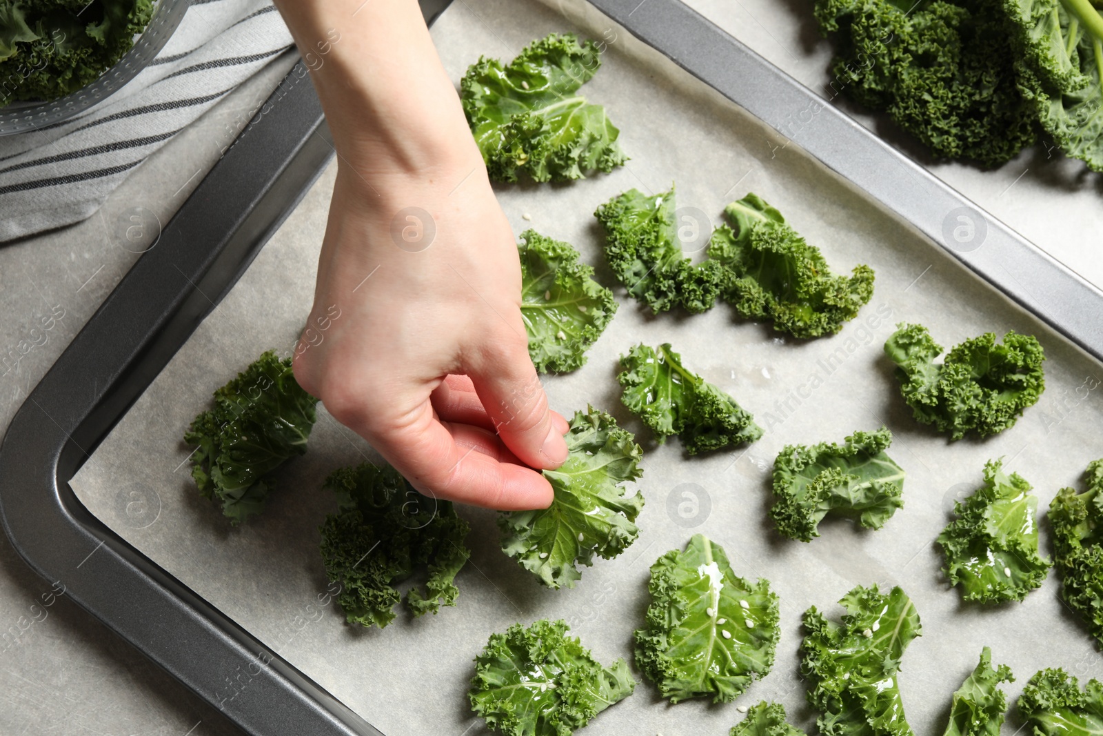 Photo of Woman preparing kale chips at table, closeup