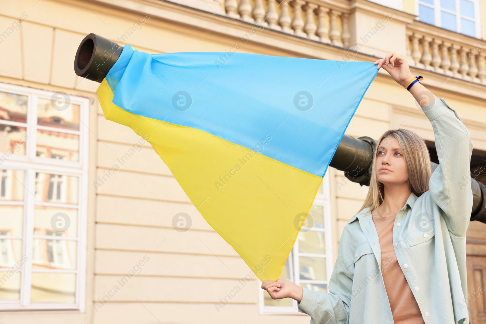 Photo of Sad woman holding Ukrainian flag near broken tank in city