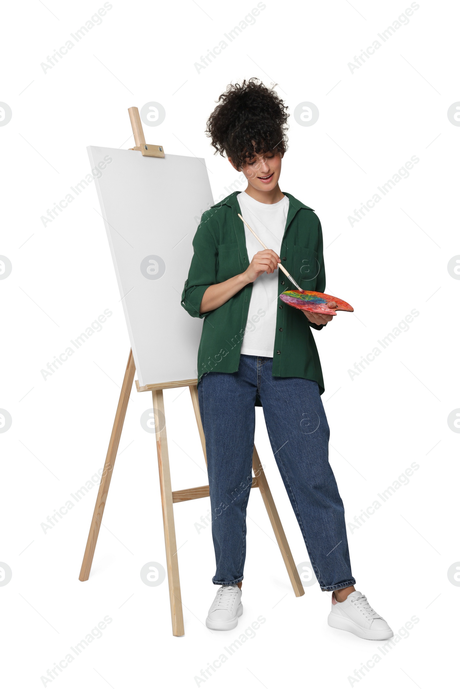 Photo of Young woman painting on easel with canvas against white background