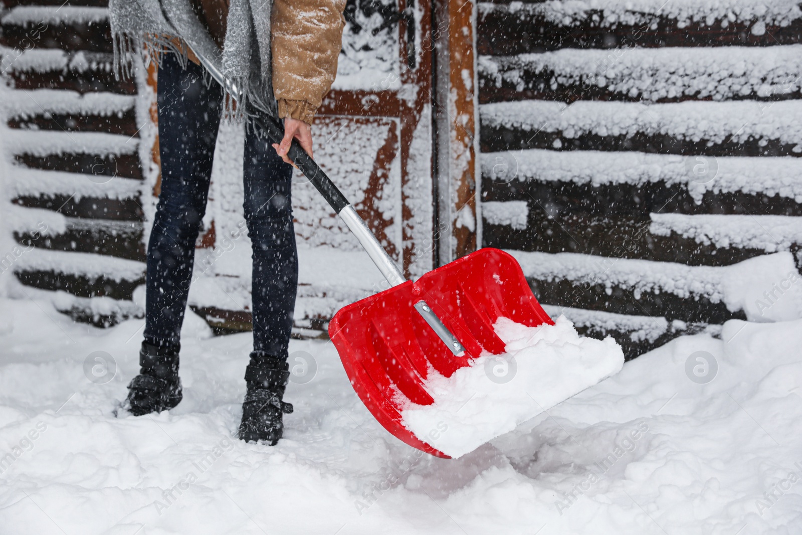 Photo of Young woman cleaning snow with shovel near her house, closeup