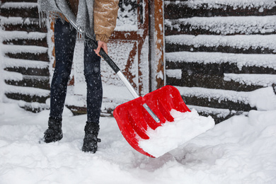 Young woman cleaning snow with shovel near her house, closeup