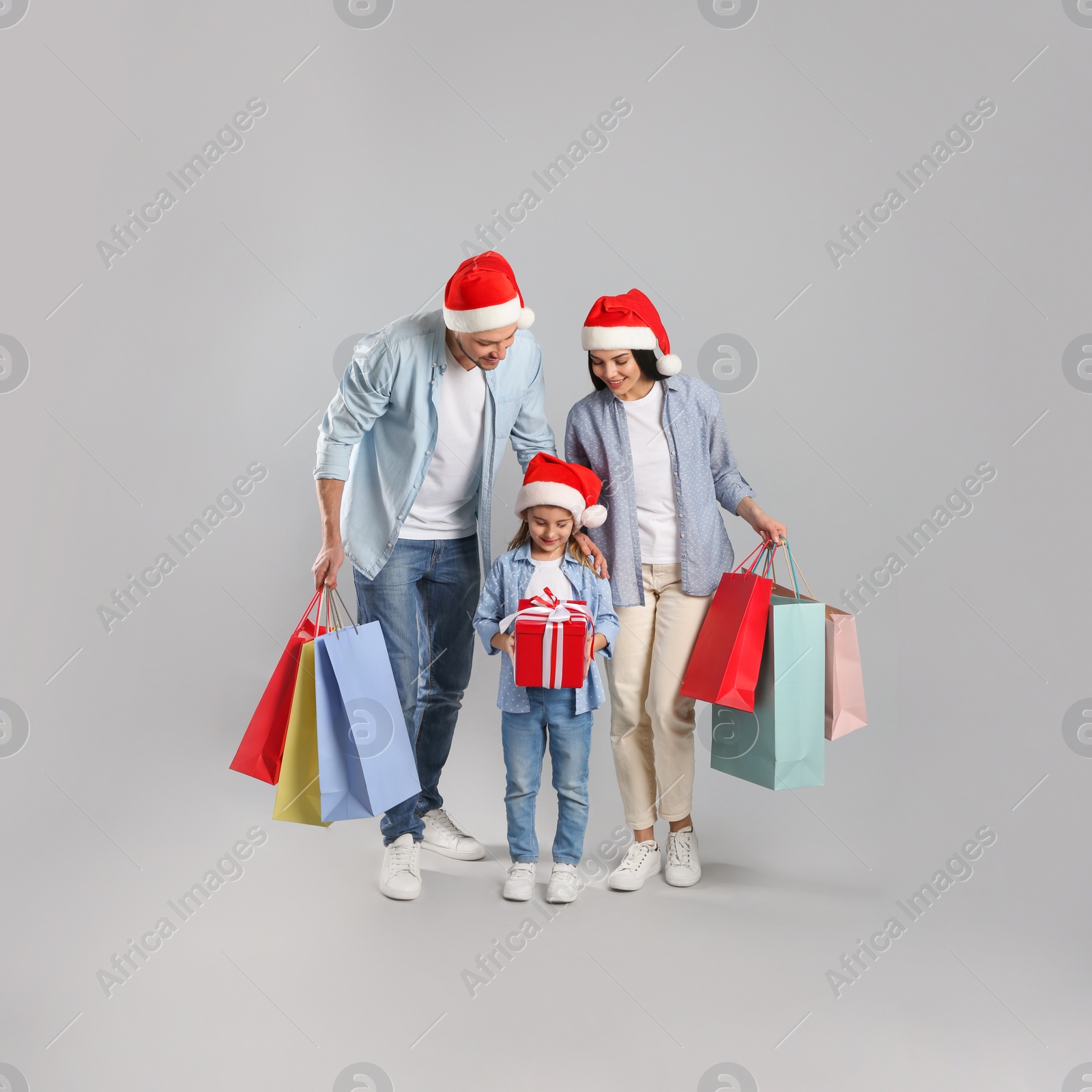 Photo of Happy family with paper bags and gift on grey background. Christmas shopping