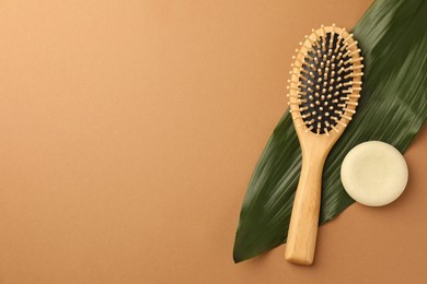 Photo of Wooden hairbrush, solid shampoo and green leaf on light brown background, flat lay. Space for text