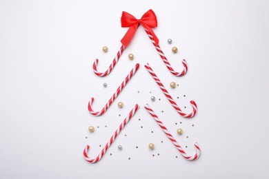 Photo of Christmas tree shape made of sweet candy canes and festive decor on white background, flat lay