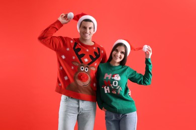 Photo of Beautiful happy couple in Santa hats and Christmas sweaters on red background