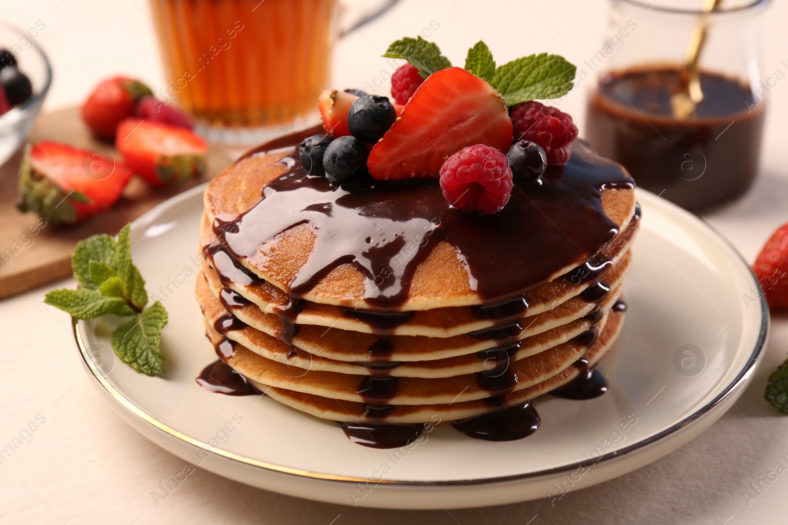 Photo of Stack of tasty pancakes with fresh berries, chocolate sauce and mint on white table, closeup