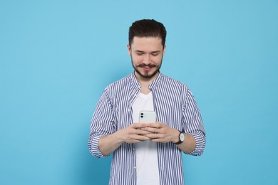 Photo of Smiling man using smartphone on light blue background