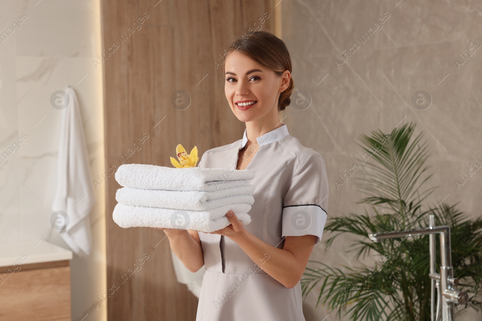 Photo of Chambermaid holding fresh towels with flower in hotel bathroom