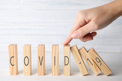 Photo of Woman stopping domino effect at white table, closeup. Prevent spreading of coronavirus