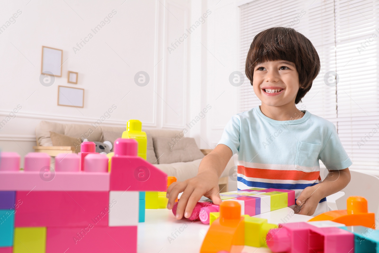 Photo of Cute little boy playing with colorful building blocks at table in living room