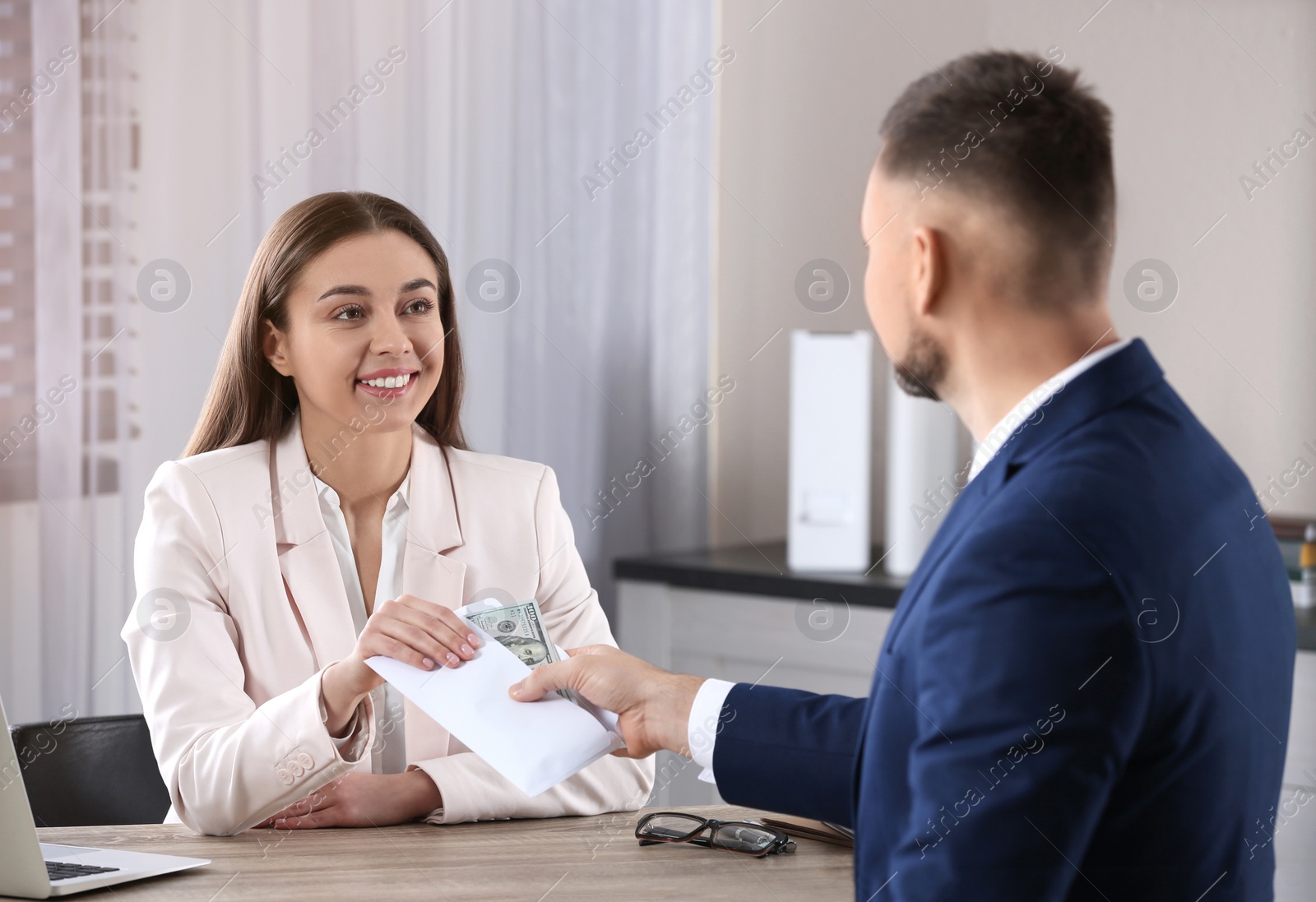 Photo of Man giving bribe to woman at table in office