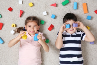 Photo of Cute children playing with colorful blocks on floor indoors, top view