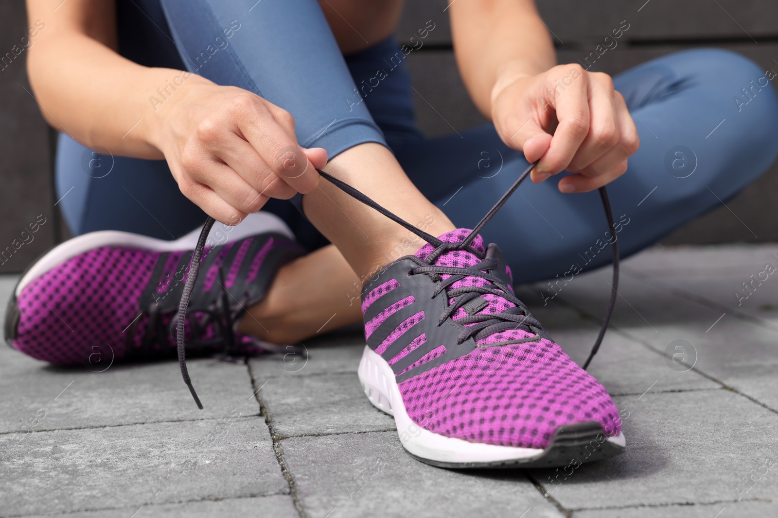 Photo of Woman tying shoelace of sneakers on street, closeup