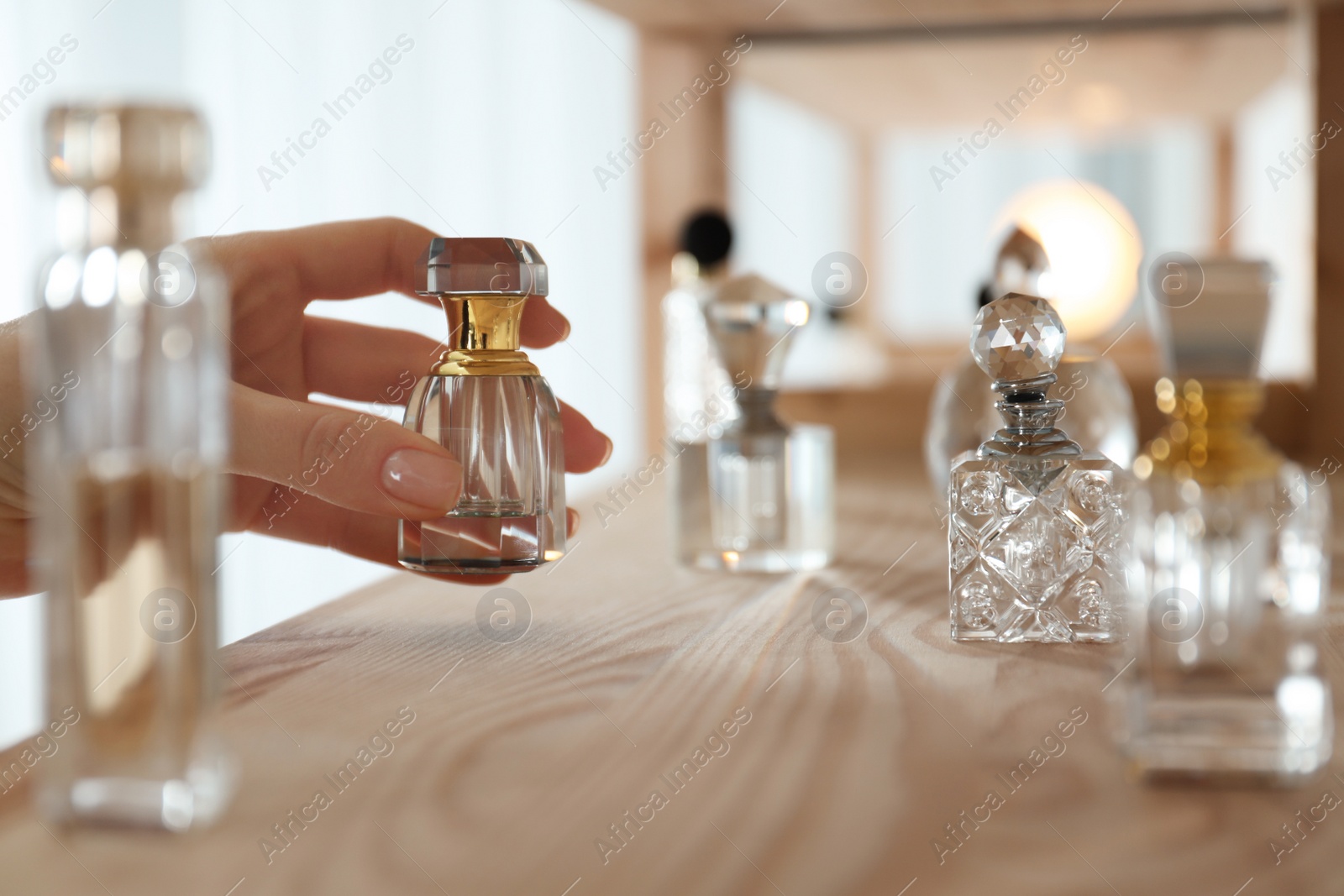 Photo of Woman taking bottle of perfume from wooden shelf indoors, closeup