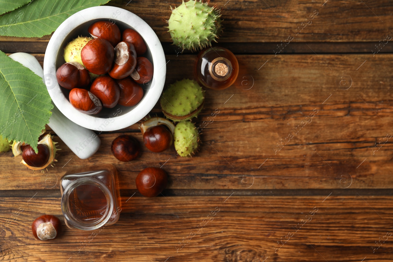 Photo of Mortar with pestle, chestnuts and essential oil on wooden table, flat lay. Space for text