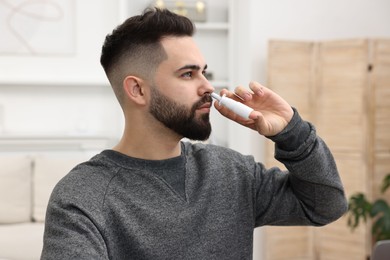 Medical drops. Young man using nasal spray indoors