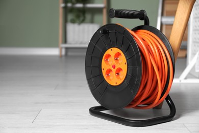 Extension cord reel on white floor in room, space for text. Electrician's equipment