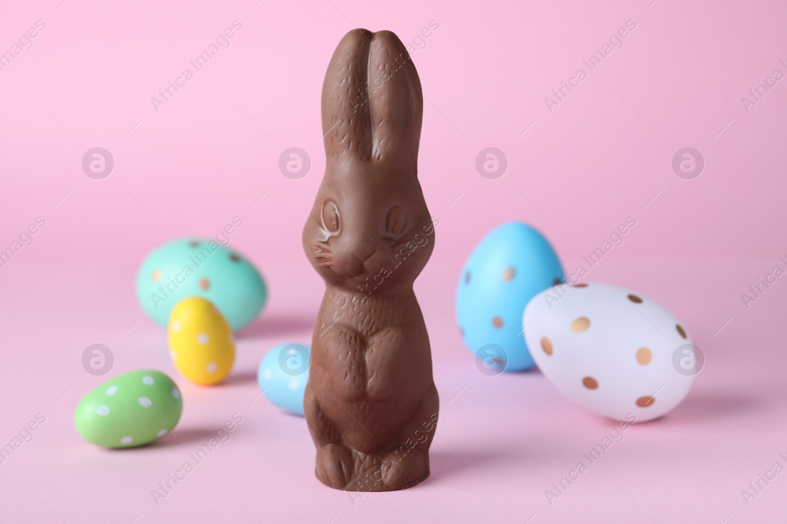 Photo of Chocolate Easter bunny and dyed eggs on pink background