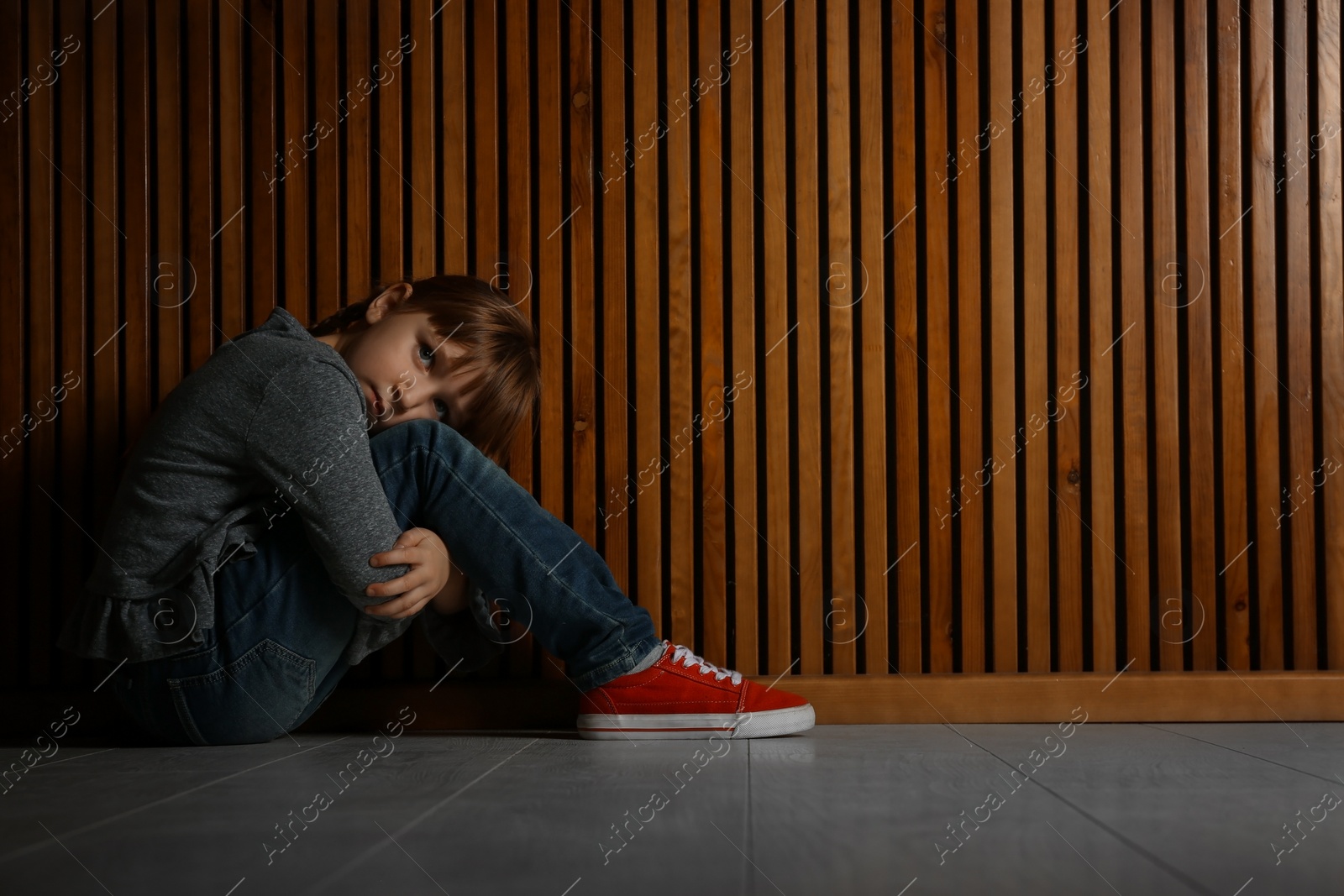 Photo of Sad little girl sitting on floor indoors, space for text. Child in danger