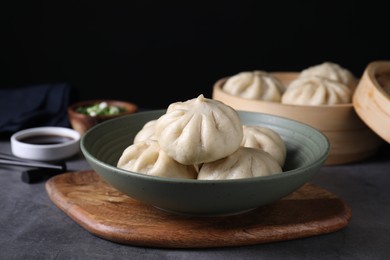 Photo of Delicious bao buns (baozi) in bowl on grey table, closeup