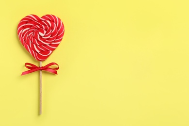 Sweet heart shaped lollipop on yellow background, top view with space for text. Valentine's day celebration