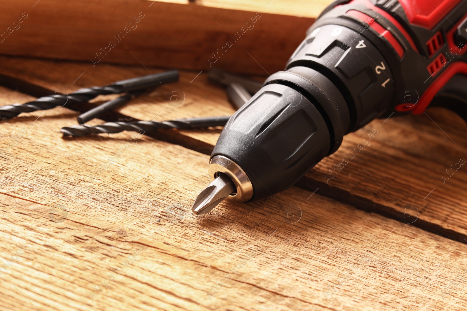 Photo of Electric screwdriver with bits and drills on wooden table, closeup