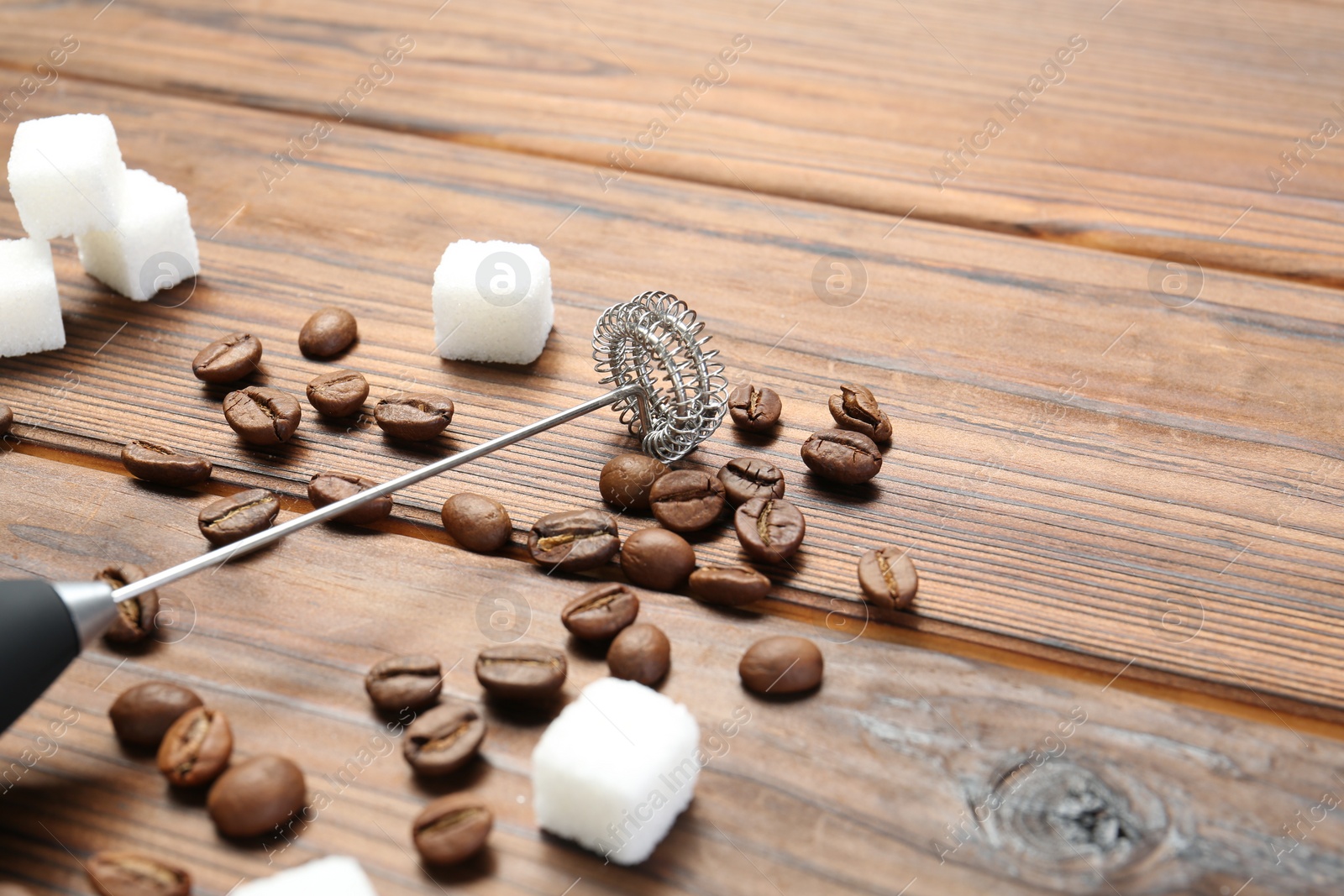 Photo of Black milk frother wand, sugar cubes and coffee beans on wooden table, closeup. Space for text