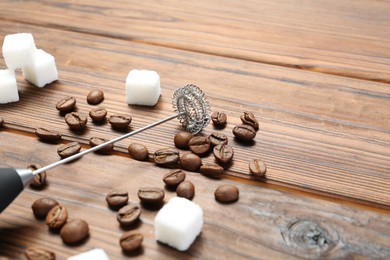 Black milk frother wand, sugar cubes and coffee beans on wooden table, closeup. Space for text